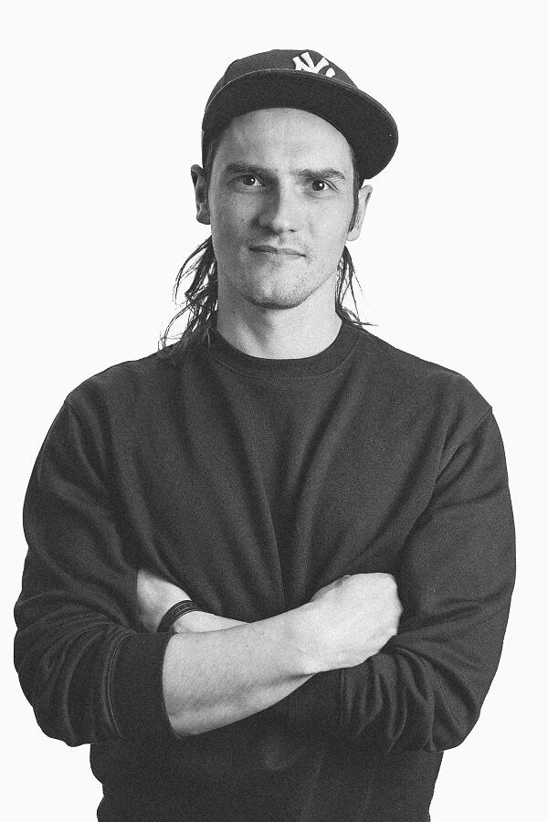 A man with long hair wearing a baseball cap, exuding a casual yet stylish vibe.